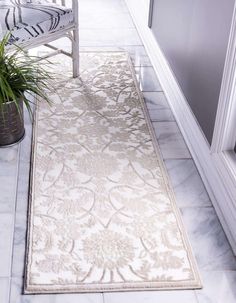 a white and beige area rug on the floor next to a chair with a potted plant