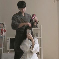 a woman is getting her hair done by a man in a kimono and holding a blow dryer