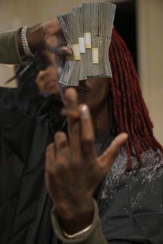 a woman with dreadlocks holding money in front of her face and making the peace sign