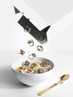 a white bowl filled with lots of different types of rings next to a gold fork