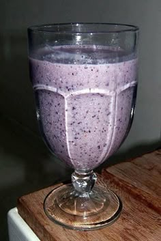 a glass filled with purple liquid sitting on top of a wooden table