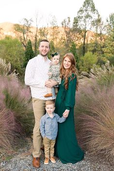 a family posing for a photo in front of some plants and bushes with their little boy