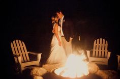 a bride and groom standing in front of a fire pit