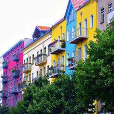 several multicolored apartment buildings line the street in front of trees and parked cars