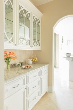 a kitchen with white cabinets and marble counter tops, along with an archway leading to the dining room