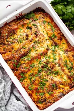 a casserole dish with meat and vegetables in it on a white cloth next to parsley