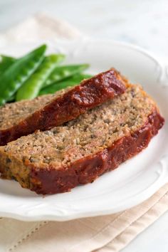 two slices of meatloaf on a white plate with green beans in the background