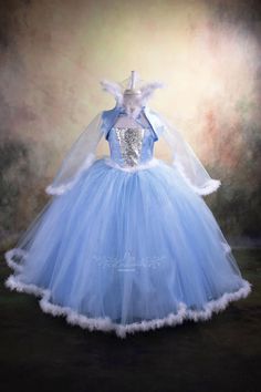 a blue and white ball gown on display in front of a dark background with light colored backdrop