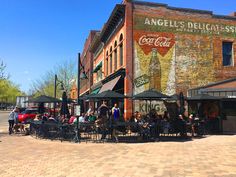 people sitting at tables in front of an old brick building on the corner of a street