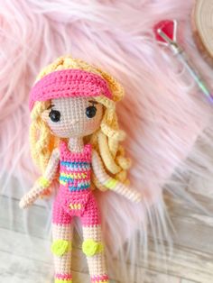 a crocheted doll is sitting on a pink furnishing next to scissors