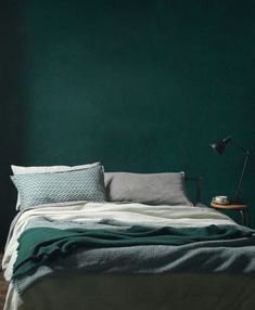 a bedroom with green walls and a bed in the foreground is a lamp on a table