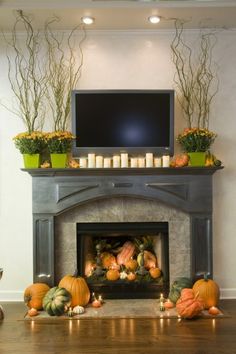 a fireplace with candles and pumpkins in front of the tv on top of it