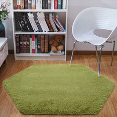 a green rug in front of a bookshelf with a white chair next to it