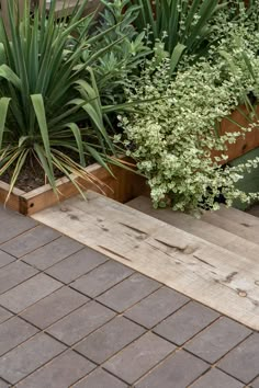 two wooden planters sitting next to each other on top of a brick floor covered in plants