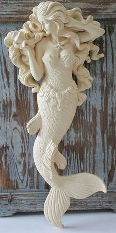 a white mermaid figurine sitting on top of a wooden table next to a wall