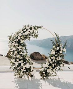 two white flowers and greenery are arranged in an arch on the ground near water