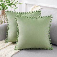 two green pillows with pom - poms on them sitting on a gray couch