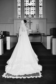 a woman in a wedding dress is looking down at her veil as she stands in front of the alter