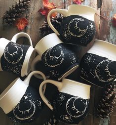 five coffee cups with moon and stars painted on them, sitting next to pine cones