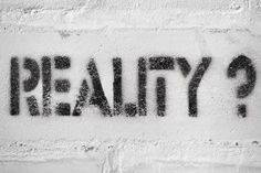 the word reality written in black spray paint on a white brick wall with question marks