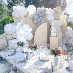 an outdoor table set with white balloons and flowers