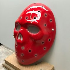 a red mask with holes on it sitting on top of a piece of plywood