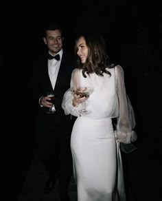 a man and woman standing next to each other holding wine glasses in front of them