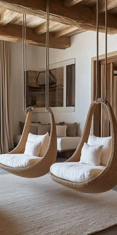 two hanging chairs in the middle of a living room with white pillows and blankets on them