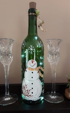 a bottle with a snowman on it next to two wine glasses and a vase