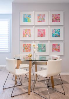 a glass table with white chairs and pictures on the wall