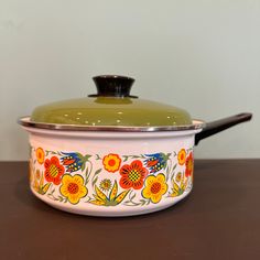 a green lid on a white pot with colorful flowers painted on the side and black handle