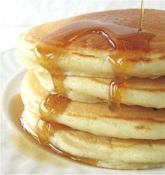 stack of pancakes covered in syrup on top of a white plate with honey drizzled over them