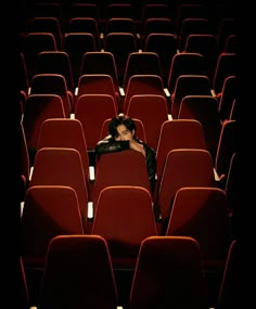 a woman sitting in an empty auditorium with her head resting on the back of a red chair