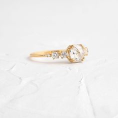 a gold ring with an oval cut diamond surrounded by three smaller round diamonds on the band