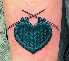 a tattoo with two knitting needles in the shape of a heart