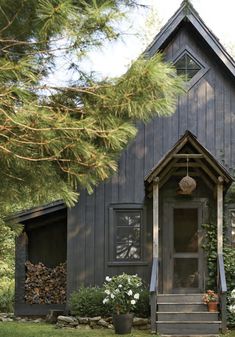 a black house with white flowers and trees in the front yard is surrounded by greenery