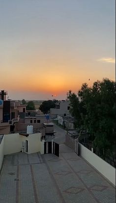 the sun is setting over some rooftops and buildings in an area with many trees