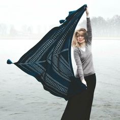 a woman holding up a blue shawl over her head in front of the water