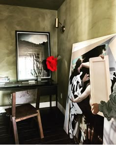 a painting is being displayed in front of a desk with a red rose on it