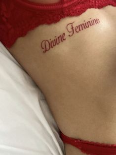 a woman with a tattoo saying divine feminine on her back, laying down in bed