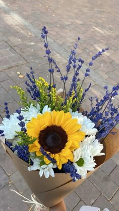 a bouquet of sunflowers and other flowers in a vase on the ground next to a brick walkway