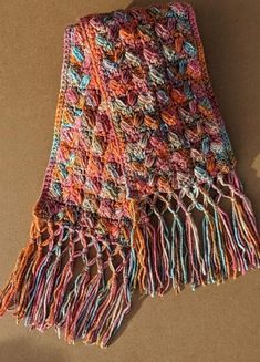 a multicolored crocheted scarf laying on top of a brown tablecloth