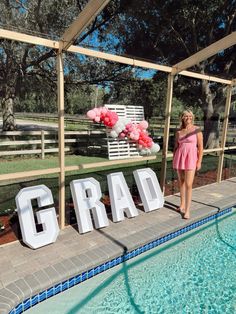 a woman standing in front of a sign that says grad next to a swimming pool