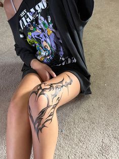 a woman sitting on the floor with her legs crossed and tattoos on her leg,