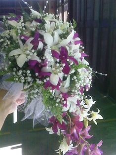 a bouquet of purple and white flowers is being held up by someone's hand