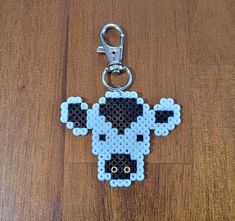 a beaded keychain shaped like a cow on a wooden surface with a metal hook