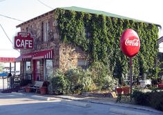 an old brick building with vines growing on it's side and a coca - cola sign in front