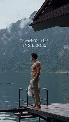 a man standing on top of a pier next to a body of water with mountains in the background