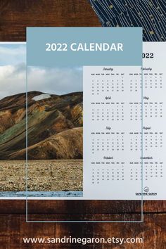 a calendar is shown on top of a wooden surface with mountains in the background and blue sky above it