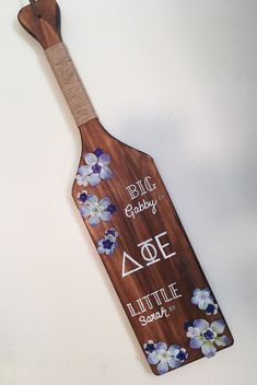 a wooden paddle with flowers on it and the words baby, one little spoon written in white